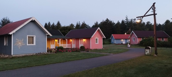 Mehrere kleine Hütten in farbiger (blau und orange) Holzoptik, an denen außen Licht brennt 
